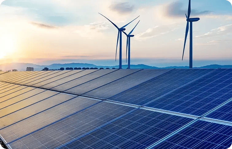 Photovoltaikmodule im Vordergrund, dahinter drei Windkraftanlagen vor einer Bergsilhouette im Abendlicht.