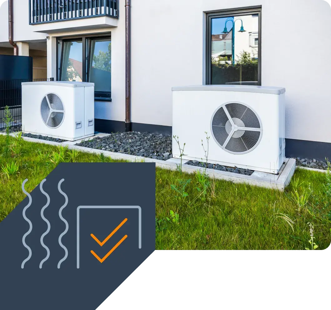 Two heat pump outdoor units on a lawn next to the façade of a residential building.