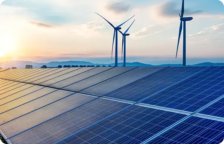   Photovoltaikmodule im Vordergrund, dahinter drei Windkraftanlagen vor einer Bergsilhouette im Abendlicht.