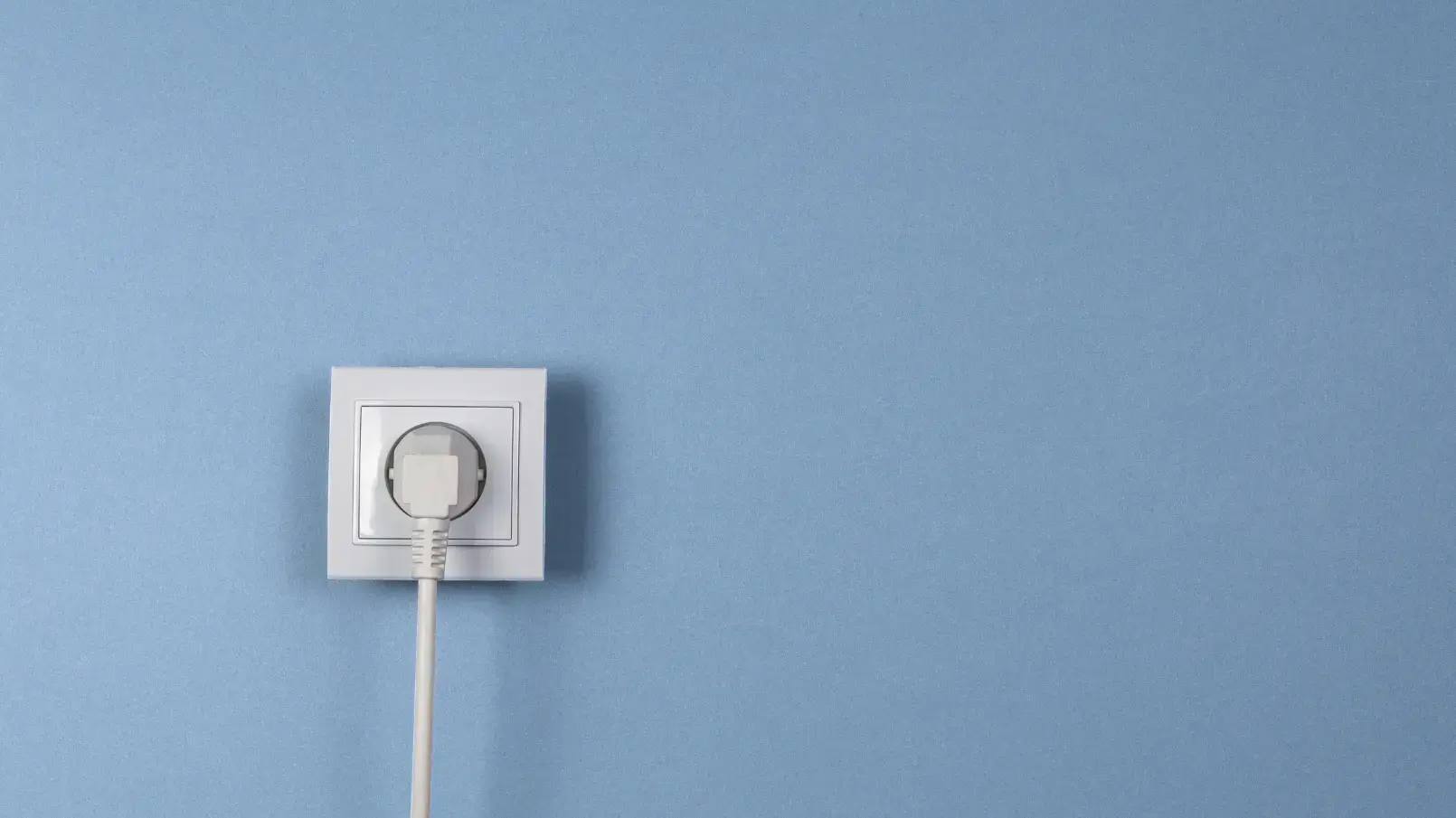 Weiße Steckdose mit eingestecktem Stecker an einer blauen Wand.